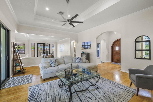 living room with ceiling fan, a raised ceiling, crown molding, and light hardwood / wood-style flooring