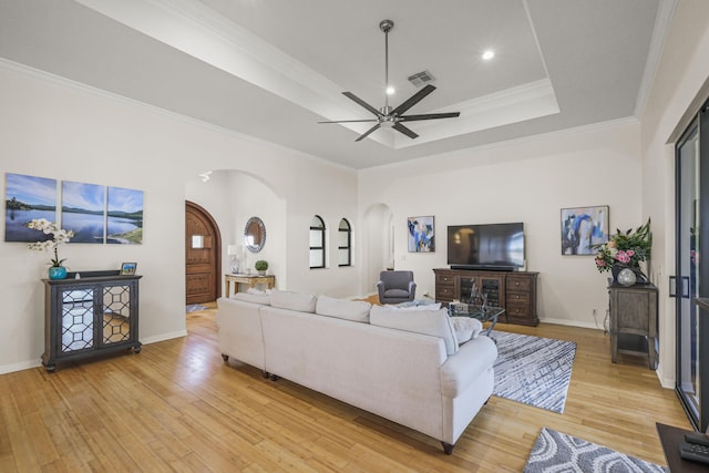 living room featuring light wood-type flooring, a tray ceiling, ceiling fan, and crown molding