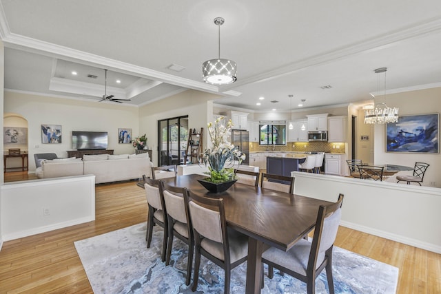 dining space featuring ceiling fan with notable chandelier, a tray ceiling, ornamental molding, and light hardwood / wood-style floors