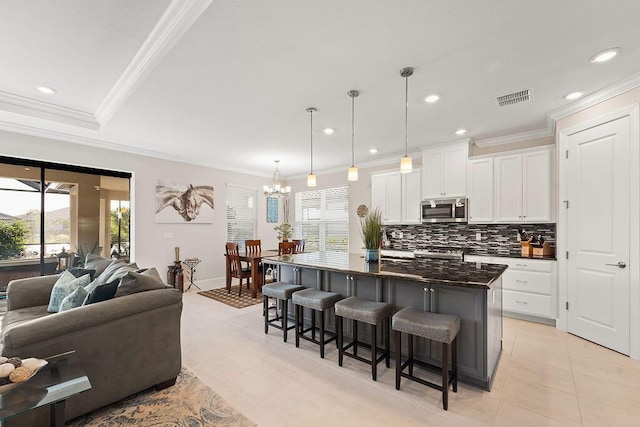 kitchen with a breakfast bar, pendant lighting, a center island with sink, white cabinets, and range