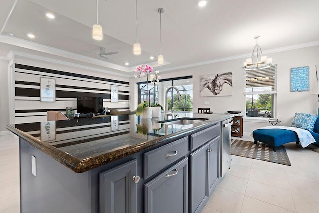 kitchen featuring a kitchen island with sink, sink, dark stone countertops, ornamental molding, and decorative light fixtures