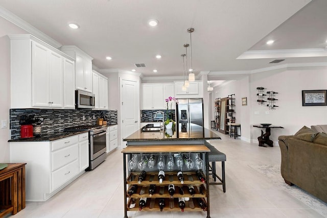 kitchen featuring decorative light fixtures, stainless steel appliances, white cabinetry, and a kitchen island with sink