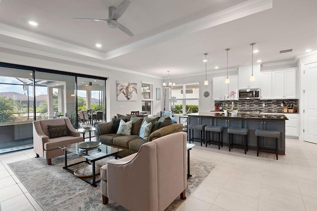 tiled living room with ceiling fan with notable chandelier, a raised ceiling, and ornamental molding