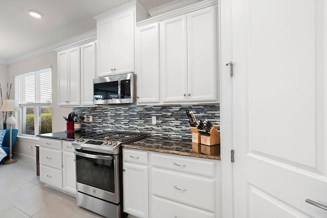 kitchen featuring tasteful backsplash, stainless steel appliances, light tile patterned floors, dark stone countertops, and white cabinetry