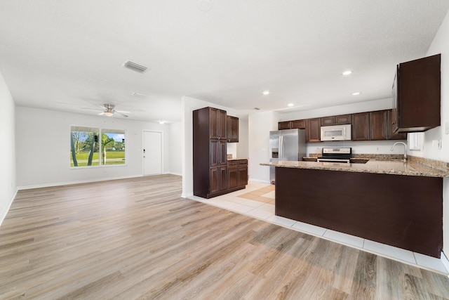 kitchen with sink, ceiling fan, light stone countertops, kitchen peninsula, and stainless steel appliances