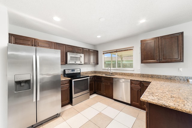 kitchen featuring dark brown cabinetry, light stone countertops, sink, light tile patterned flooring, and appliances with stainless steel finishes