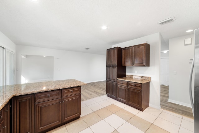 kitchen with light tile patterned flooring, dark brown cabinetry, and light stone countertops