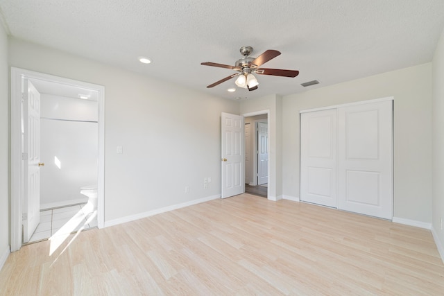 unfurnished bedroom featuring connected bathroom, ceiling fan, light hardwood / wood-style floors, a textured ceiling, and a closet