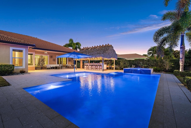 pool at dusk featuring a gazebo, a patio area, pool water feature, and a hot tub