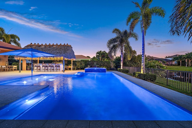 pool at dusk featuring pool water feature and an outdoor bar