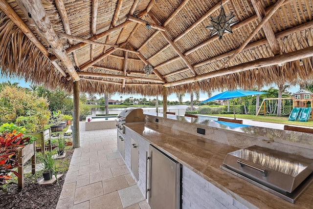 view of patio featuring a playground, a gazebo, an outdoor kitchen, and a grill