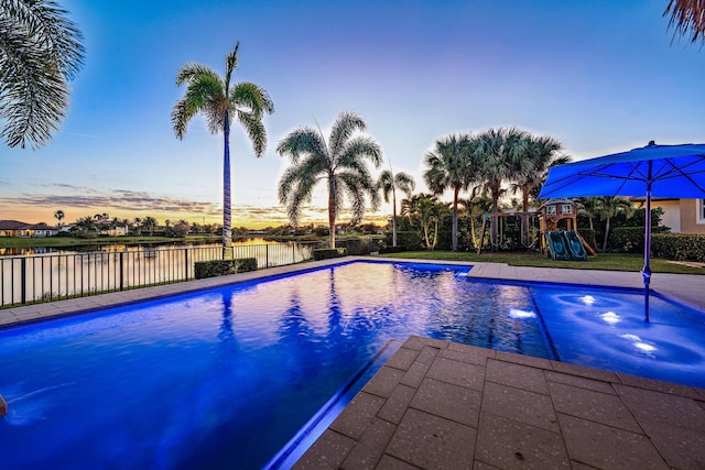 pool at dusk featuring a water view and a playground