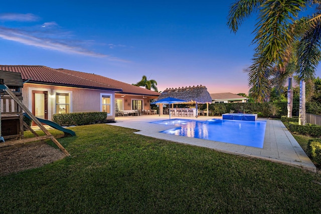 pool at dusk featuring a patio, a lawn, and pool water feature