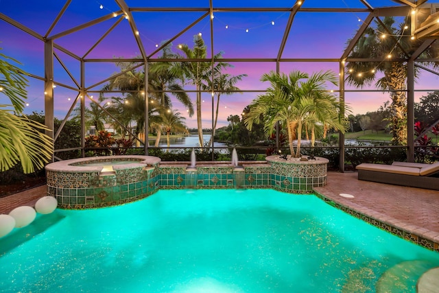 pool at dusk with an in ground hot tub, pool water feature, a water view, glass enclosure, and a patio