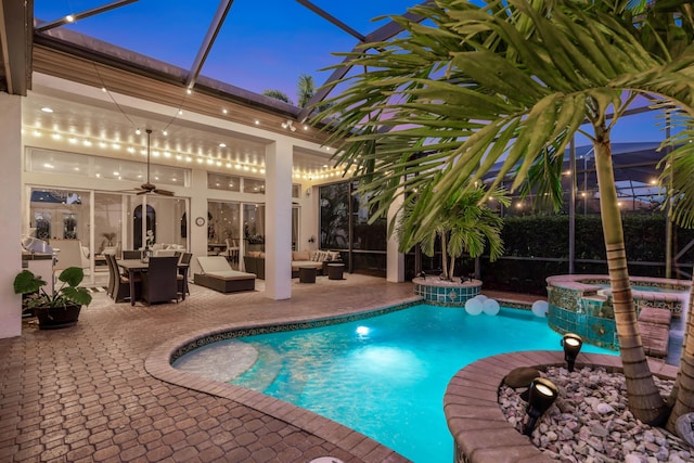 pool at dusk featuring outdoor lounge area, ceiling fan, a lanai, a patio area, and an in ground hot tub