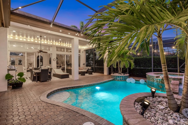 pool at dusk featuring outdoor lounge area, ceiling fan, a lanai, a patio area, and an in ground hot tub