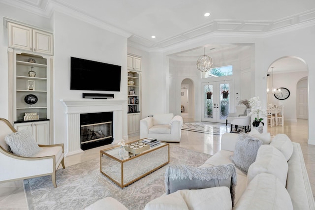 tiled living room featuring built in features, ornamental molding, a high ceiling, and a notable chandelier