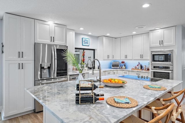 kitchen with stainless steel appliances, light stone counters, and white cabinetry