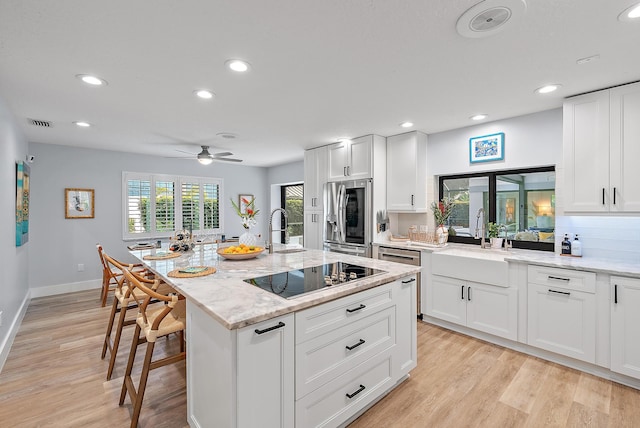 kitchen featuring white cabinetry, stainless steel appliances, light stone counters, light hardwood / wood-style floors, and a kitchen island with sink