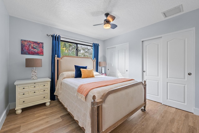 bedroom featuring ceiling fan, light wood-type flooring, a textured ceiling, and multiple closets