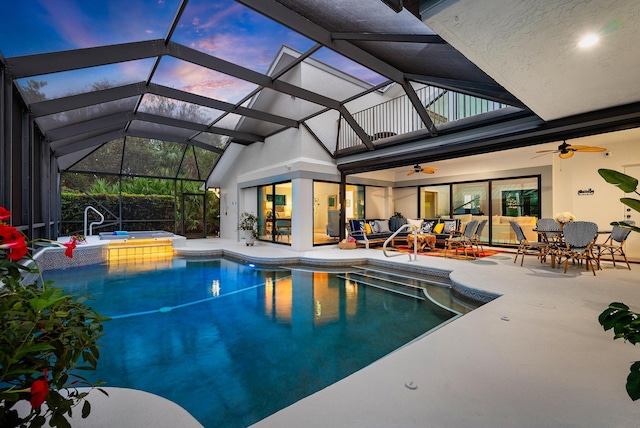 pool at dusk with an in ground hot tub, a lanai, outdoor lounge area, ceiling fan, and a patio