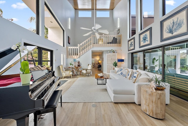 living room featuring ceiling fan, a healthy amount of sunlight, light hardwood / wood-style floors, and a high ceiling