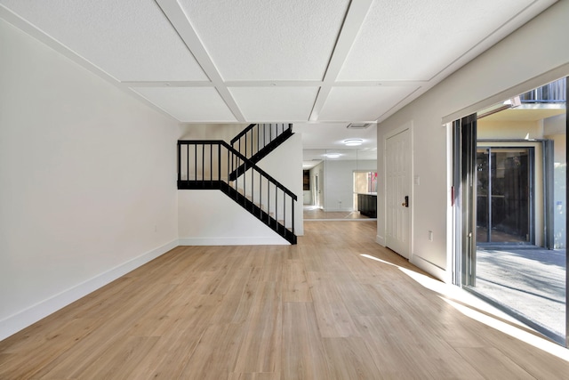 interior space with a textured ceiling, coffered ceiling, and light wood-type flooring