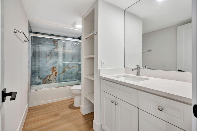 full bathroom with combined bath / shower with glass door, hardwood / wood-style floors, vanity, and toilet