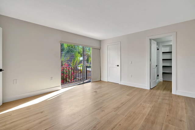 unfurnished bedroom with a walk in closet, access to outside, light hardwood / wood-style flooring, and a closet