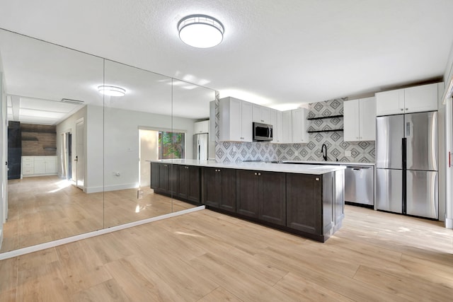 kitchen with dark brown cabinetry, a center island, appliances with stainless steel finishes, white cabinets, and light wood-type flooring