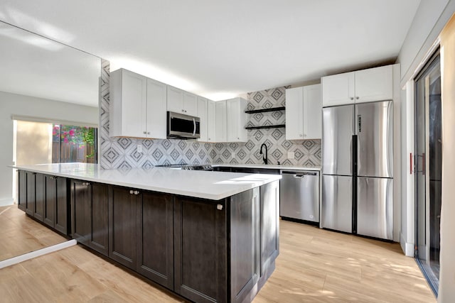 kitchen with dark brown cabinets, light hardwood / wood-style floors, appliances with stainless steel finishes, and tasteful backsplash