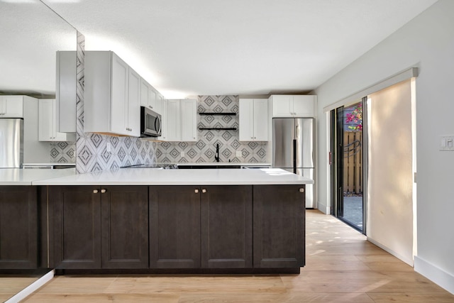 kitchen with stainless steel appliances, light hardwood / wood-style floors, decorative backsplash, dark brown cabinets, and white cabinets