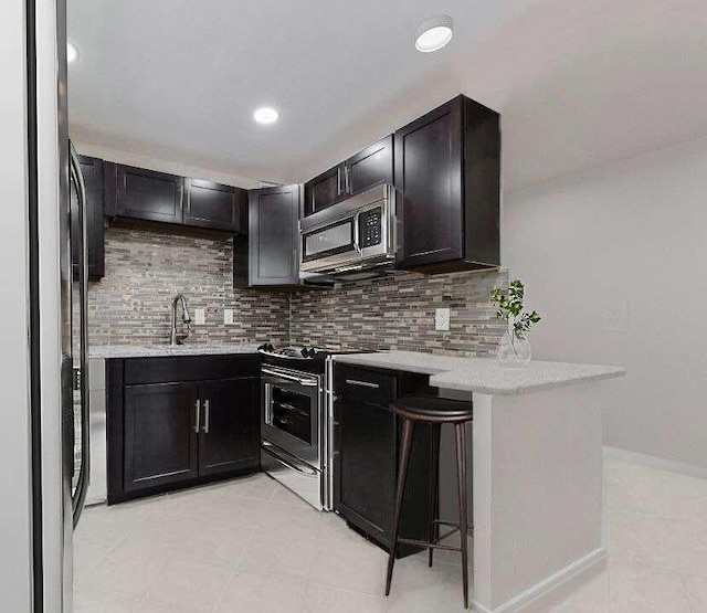 kitchen with a kitchen breakfast bar, light tile patterned floors, appliances with stainless steel finishes, tasteful backsplash, and kitchen peninsula