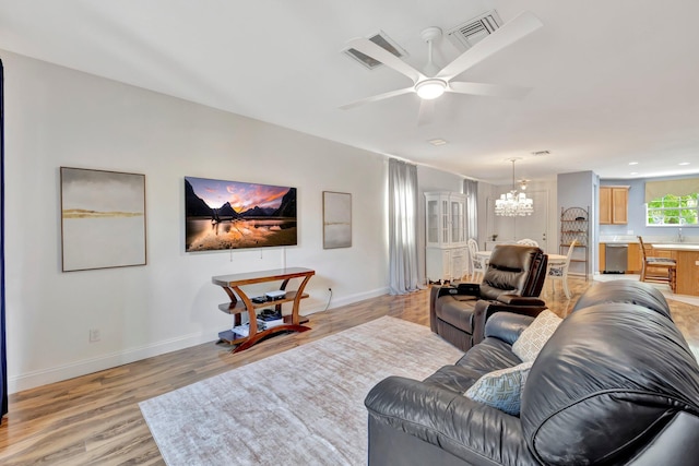 living room with ceiling fan with notable chandelier, visible vents, light wood-style flooring, and baseboards