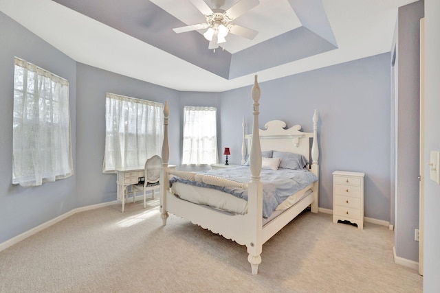 carpeted bedroom with a raised ceiling and ceiling fan