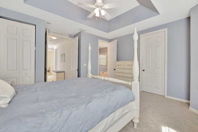 bedroom featuring a tray ceiling, connected bathroom, ceiling fan, and carpet flooring