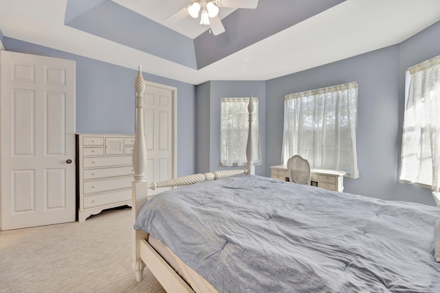 bedroom featuring a raised ceiling, light carpet, multiple windows, and ceiling fan