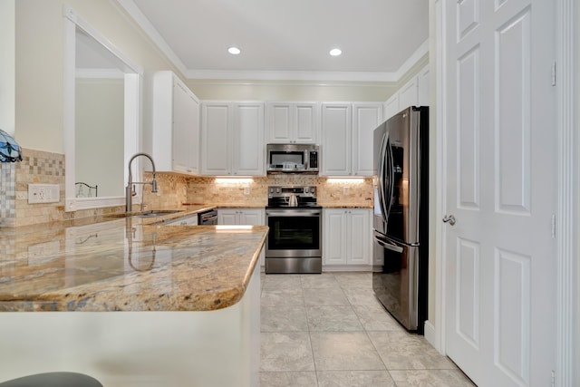 kitchen with kitchen peninsula, appliances with stainless steel finishes, light stone counters, sink, and white cabinetry