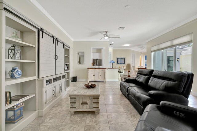 tiled living room featuring built in shelves, a barn door, ceiling fan, and crown molding