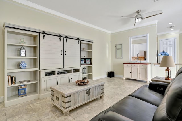 living room with a barn door, built in features, ceiling fan, and crown molding