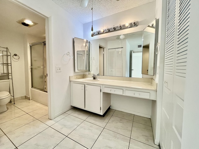 full bathroom with ceiling fan, a textured ceiling, toilet, shower / bath combination with glass door, and vanity