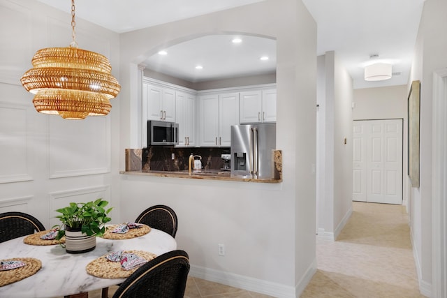 kitchen with backsplash, decorative light fixtures, white cabinetry, kitchen peninsula, and stainless steel appliances