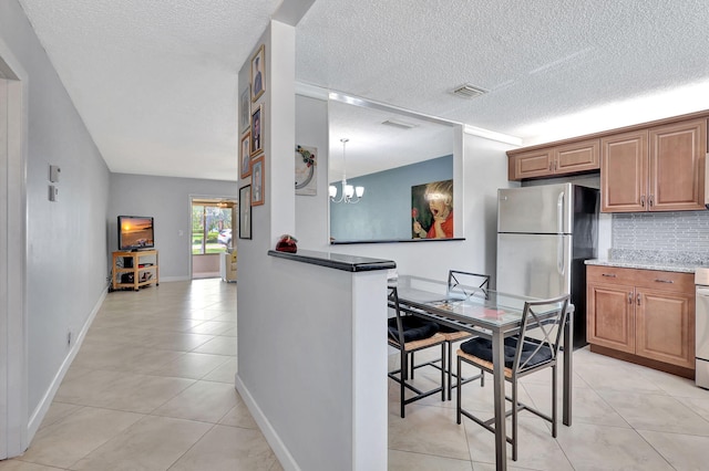 kitchen with stainless steel fridge, light tile patterned floors, a textured ceiling, tasteful backsplash, and a chandelier