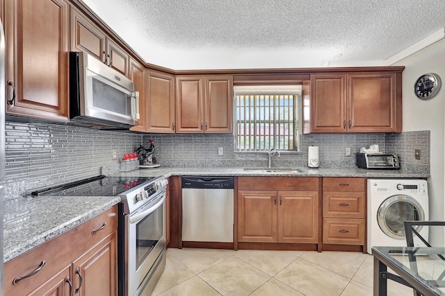 kitchen with light stone counters, stainless steel appliances, sink, light tile patterned floors, and washer / dryer