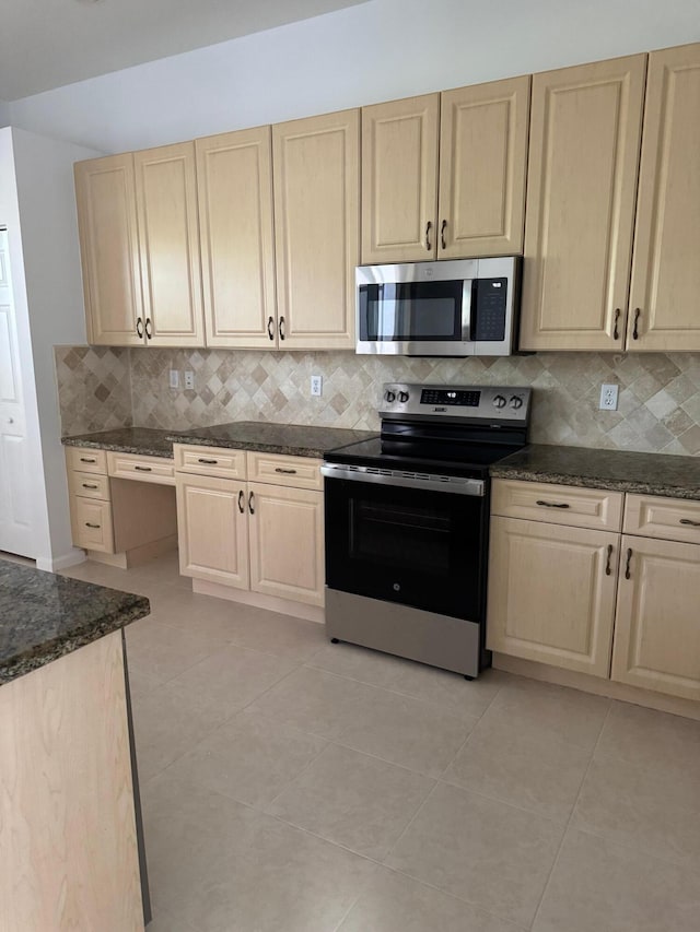 kitchen with appliances with stainless steel finishes, backsplash, light tile patterned floors, and dark stone counters