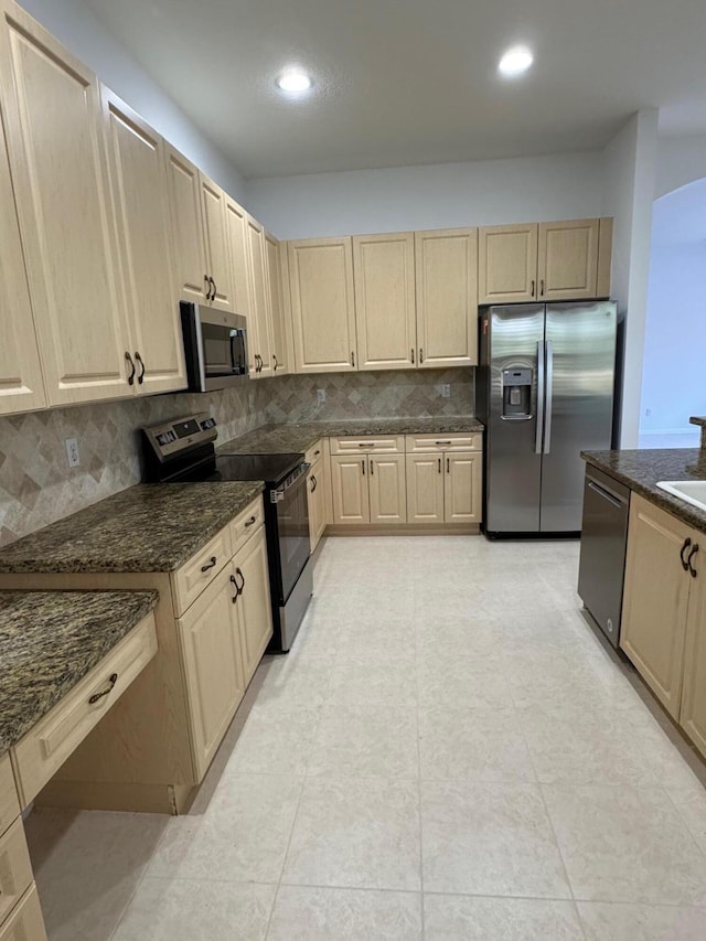 kitchen with decorative backsplash, light brown cabinets, stainless steel appliances, and dark stone countertops