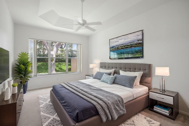 bedroom with a raised ceiling, ceiling fan, and light carpet