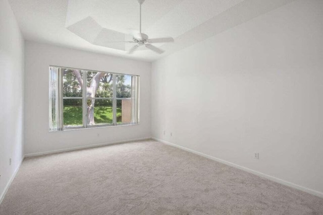 unfurnished room with a tray ceiling, ceiling fan, and light carpet