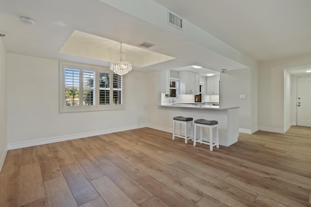 kitchen with light wood-style flooring, visible vents, a raised ceiling, and decorative backsplash