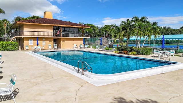 view of pool with tennis court and a patio area